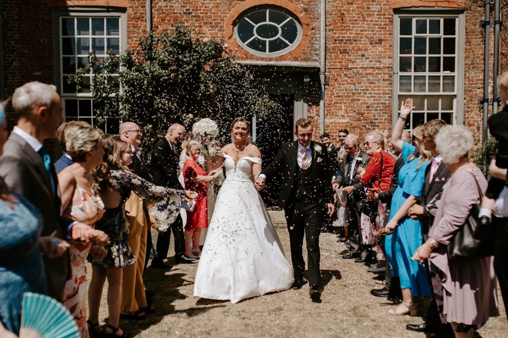 bride and groom walking through confetti line at Glemham Hall