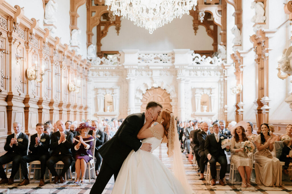 bride and groom first kiss in great hall at harlaxton manor wedding venue