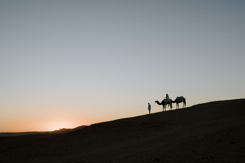 couple eloping riding camels into sunset on sand dune in the agafay desert