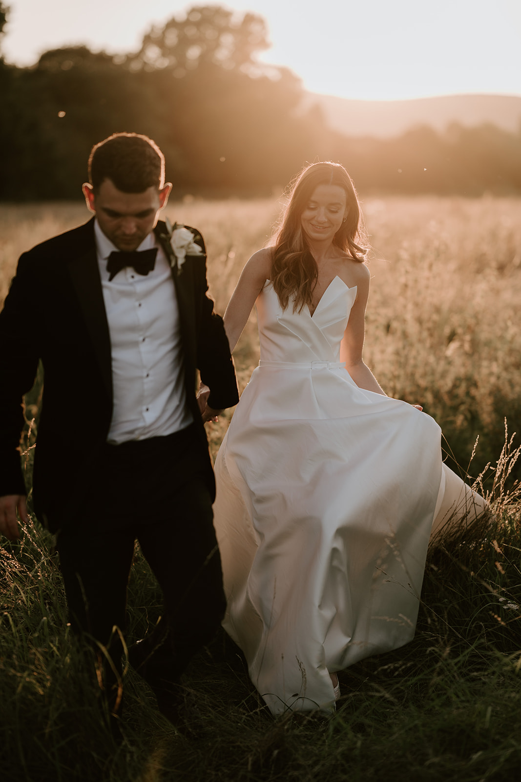 bride and groom walking through fields at golden hour