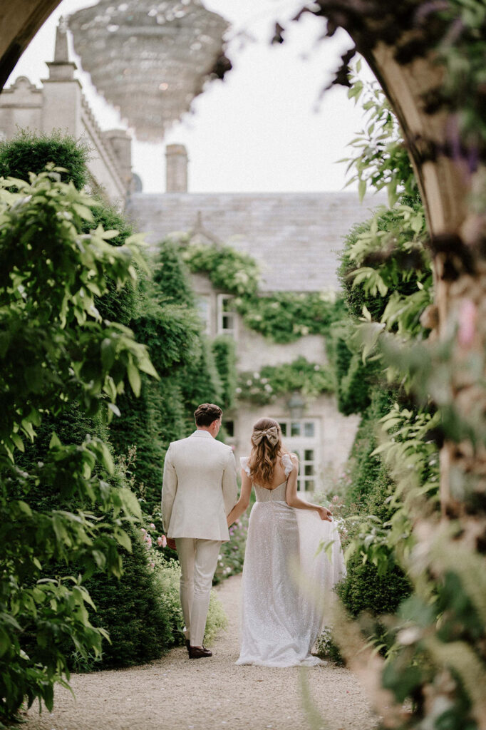 bride and groom walking through gardens at euridge manor. bride Is wearing bow in hair