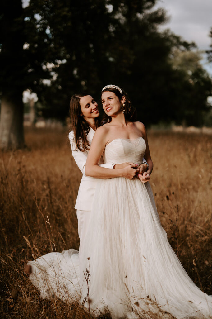two brides in field hugging each other