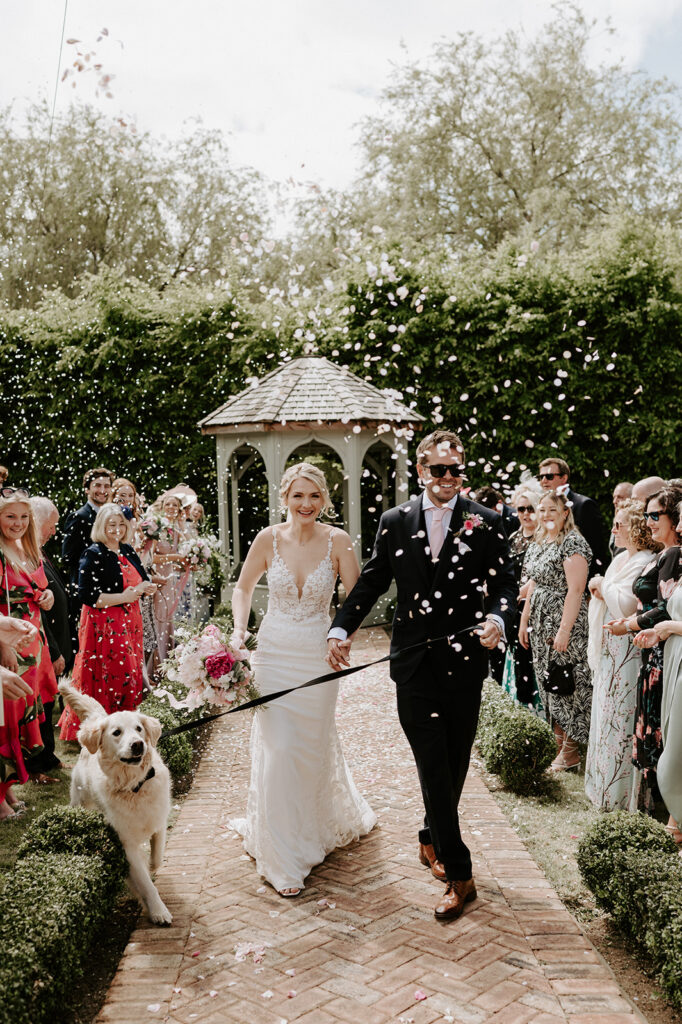 couple walking back down aisle with their dog and confetti being thrown by guests at retreat east