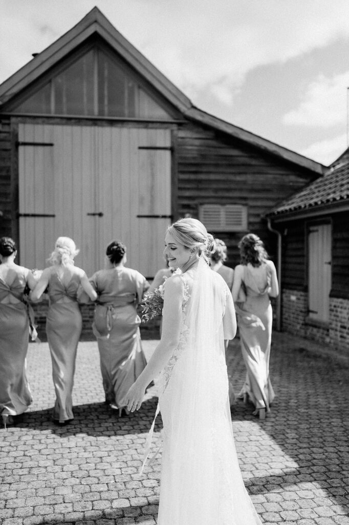 bride wearing long veil walking away with bridesmaids