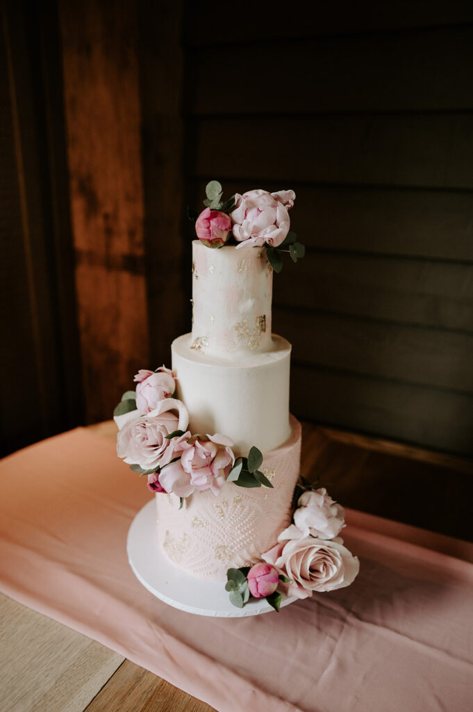 white and pink wedding cake in the great barn at retreat east