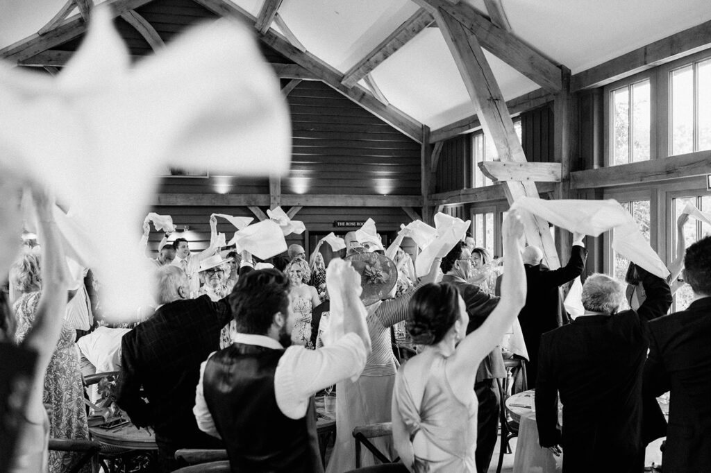 wedding guests waving napkins and couple enter reception in the great barn 