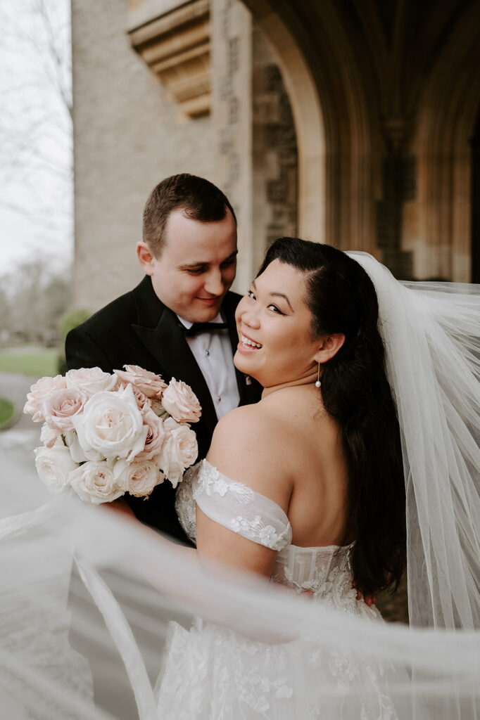 bride and groom with veil floating in wind holding blush pink rose bouquet
