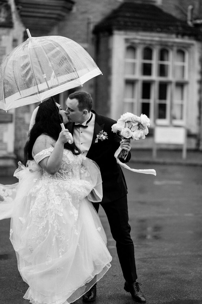 bride and groom sharing a kiss with clear umbrella walking in the rain at tortworth court