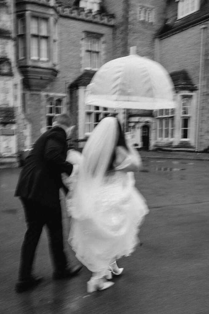 bride and groom with clear umbrella walking in the rain at tortworth court